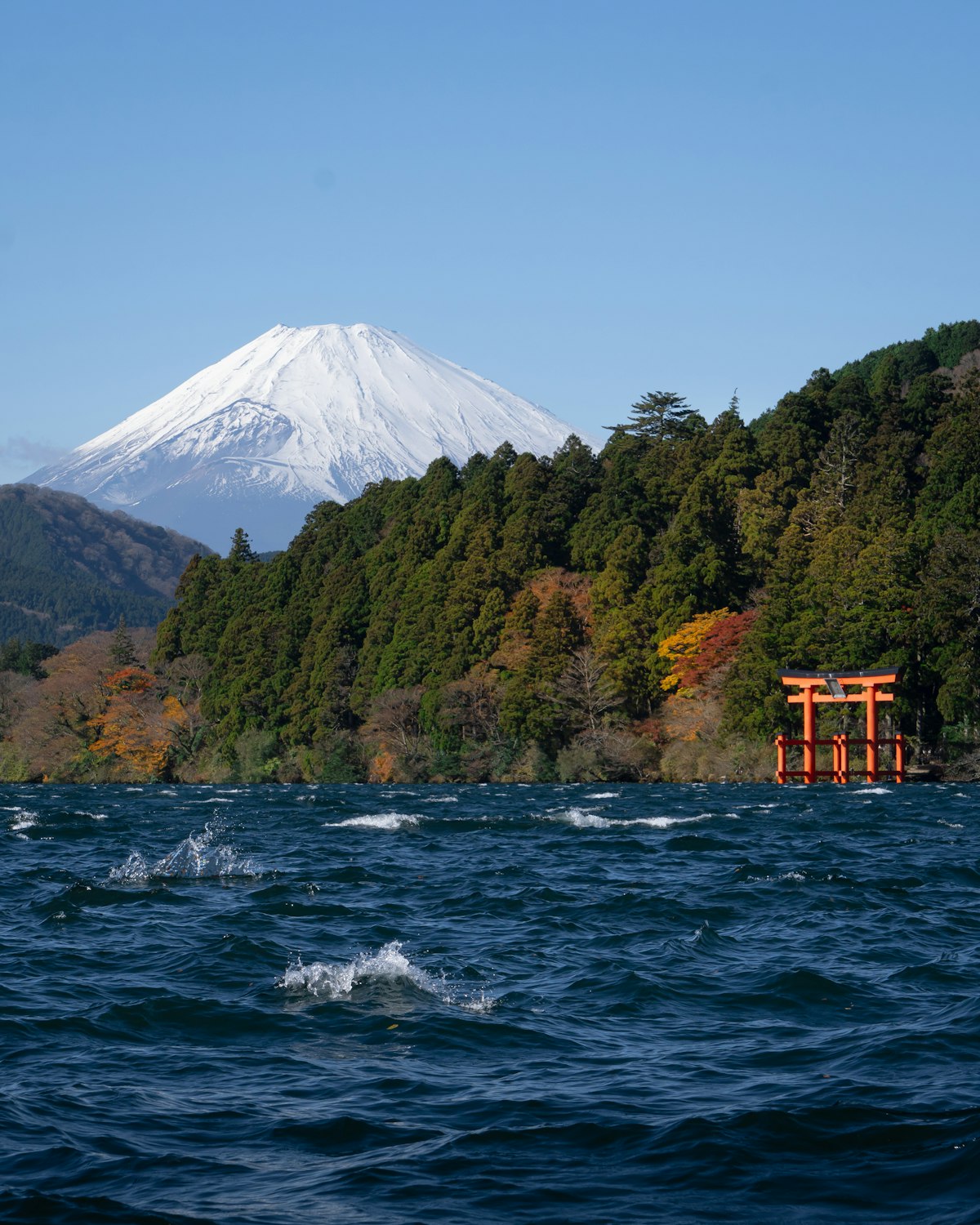 Mount Fuji above Lake Ashi with the red torii gate of Hakone Shrine at the wooded shoreline